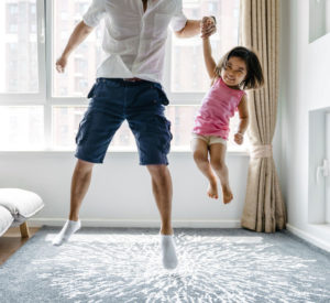a man jumps holding his young smiling daughter by the hand