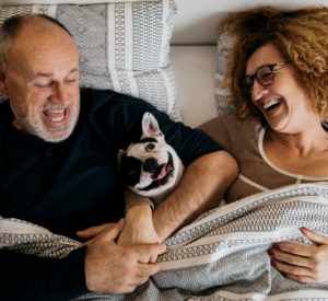 older couple laughs in bed with silly dog