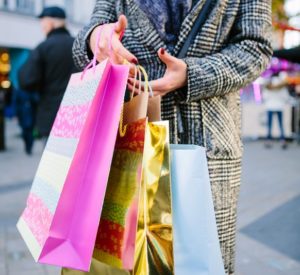woman in peacoat carries brightly colored shopping bags